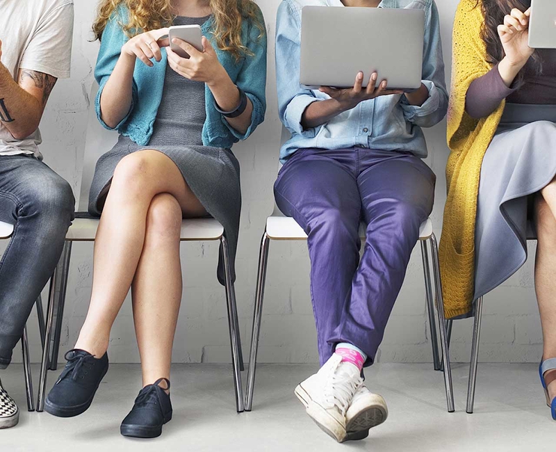 Menschen in unterschiedlicher Kleidung sitzen und bedienen mobile Geräte, Köpfe sind nicht im Bild zu sehen.